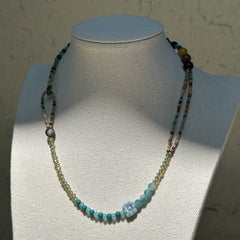 Aqua Loop Blossom Necklace worn on bust, highlighting asymmetrical double-loop side detail with aqua and gold beads and floral glass centerpiece