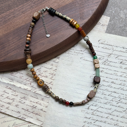Desert Caravan Necklace close-up on wooden surface, featuring warm desert palette of sand, terracotta, olive, and teal with wood, ceramic, and glass beads