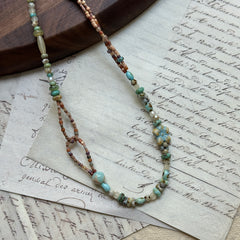 Sage Loop Blossom Necklace close-up on rustic paper, featuring floral Czech-glass focal, sage and mint beads, sandy peach tones, and double-loop detail