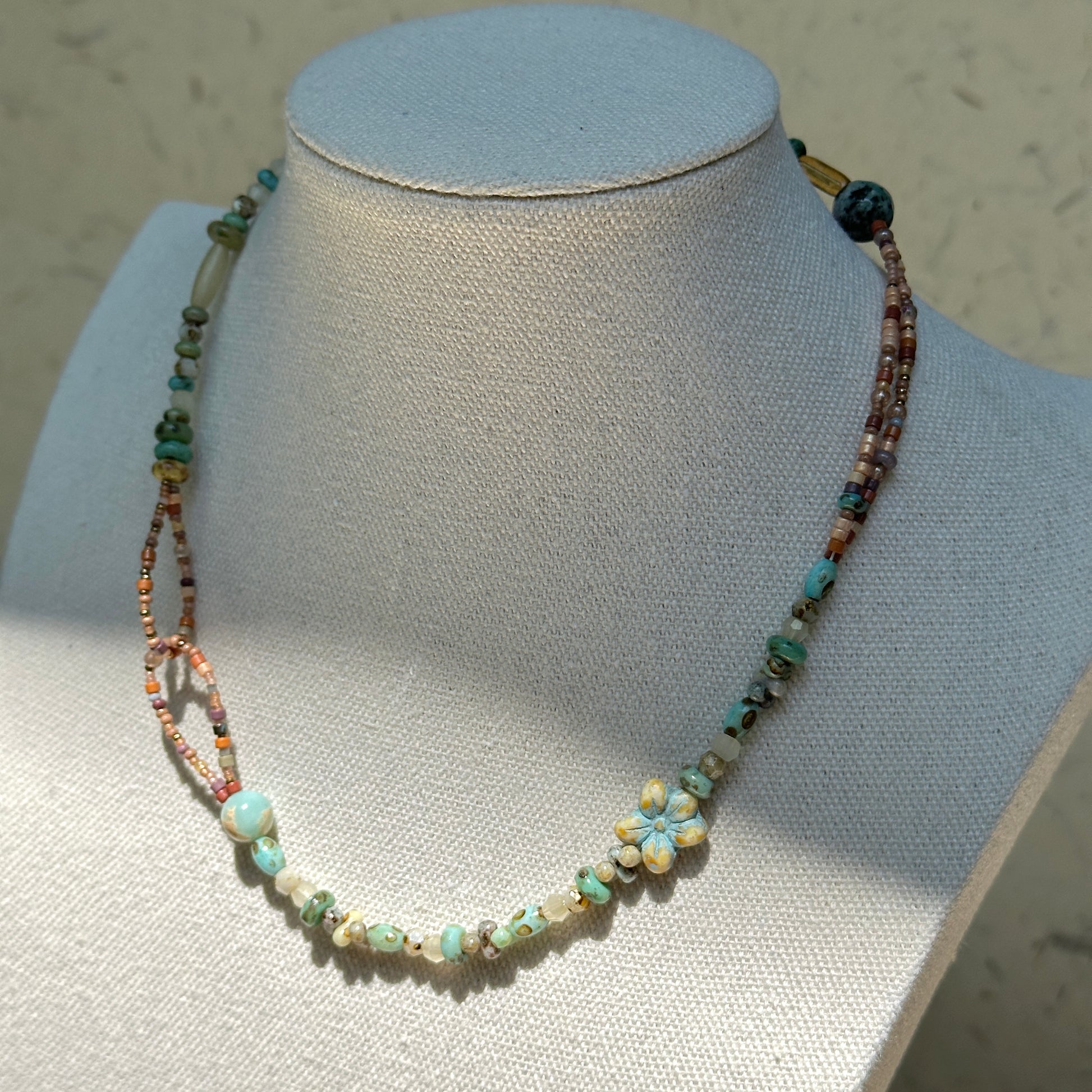 Sage Loop Blossom Necklace worn on bust, highlighting modern double-loop side detail, sage and peach beads, and Czech-glass floral focal