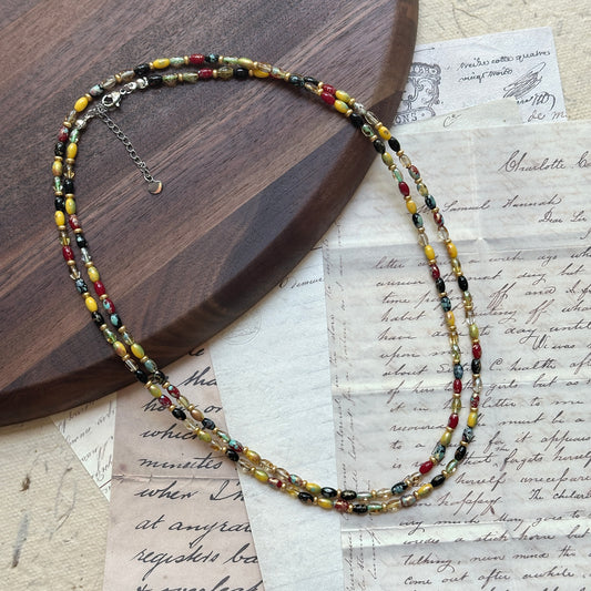 Tribal Glow Necklace close-up on rustic paper, featuring vibrant glass beads in red, yellow, green, and black with double-layer design