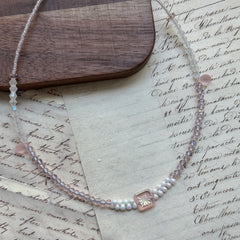 Blush Crystal Necklace close-up on rustic surface, featuring square bezel-set crystal centerpiece with blush pink and clear beads