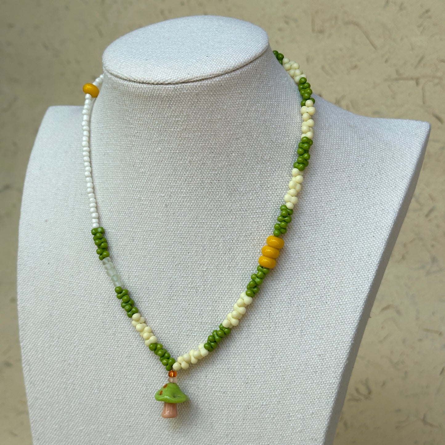 Forest Mushroom Necklace worn on bust, highlighting glass mushroom charm with lively green and ivory bead palette