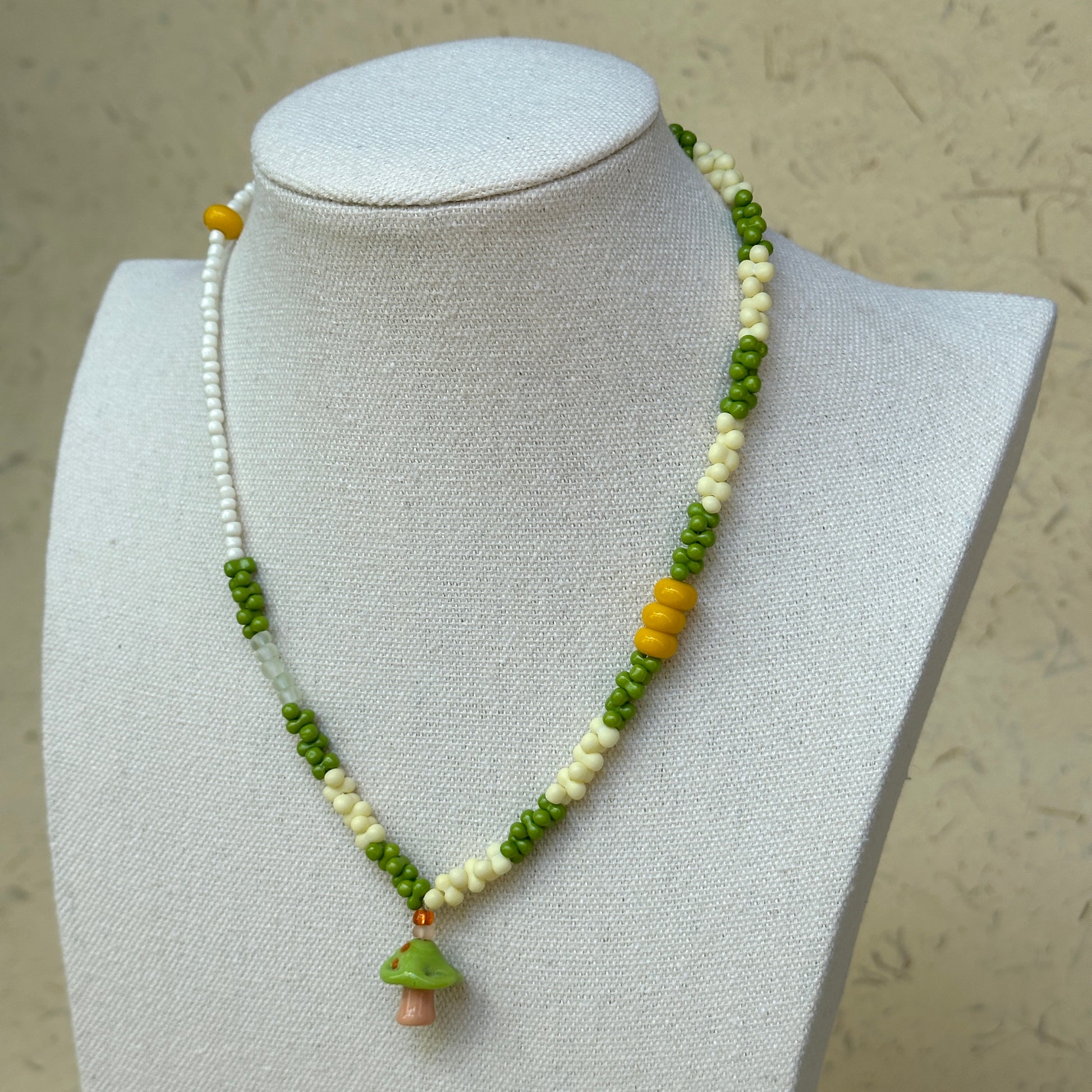 Forest Mushroom Necklace worn on bust, highlighting glass mushroom charm with lively green and ivory bead palette
