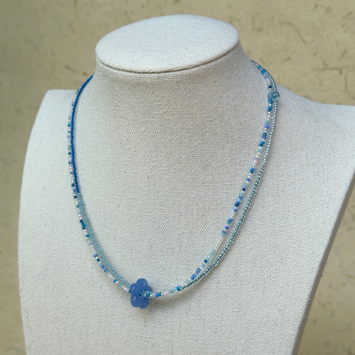 Azure Bloom Necklace worn on bust, highlighting azure glass flower pendant with minimal beaded silhouette in blue and white
