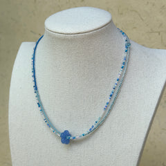 Azure Bloom Necklace worn on bust, highlighting azure glass flower pendant with minimal beaded silhouette in blue and white
