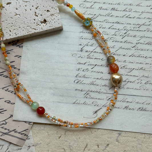Golden Ember Necklace close-up on rustic paper, featuring radiant amber-orange and gold beads with warm ember tones