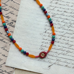 Sunburst Fiesta Necklace close-up on rustic paper, featuring multicolor glass beads in vibrant red, orange, turquoise, and blue tones