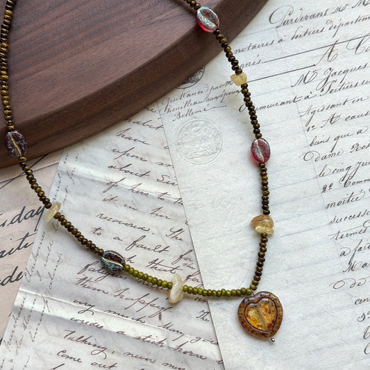Aurora Heart Necklace close-up on rustic paper, featuring multicolor glass beads with golden accents and glowing heart pendant