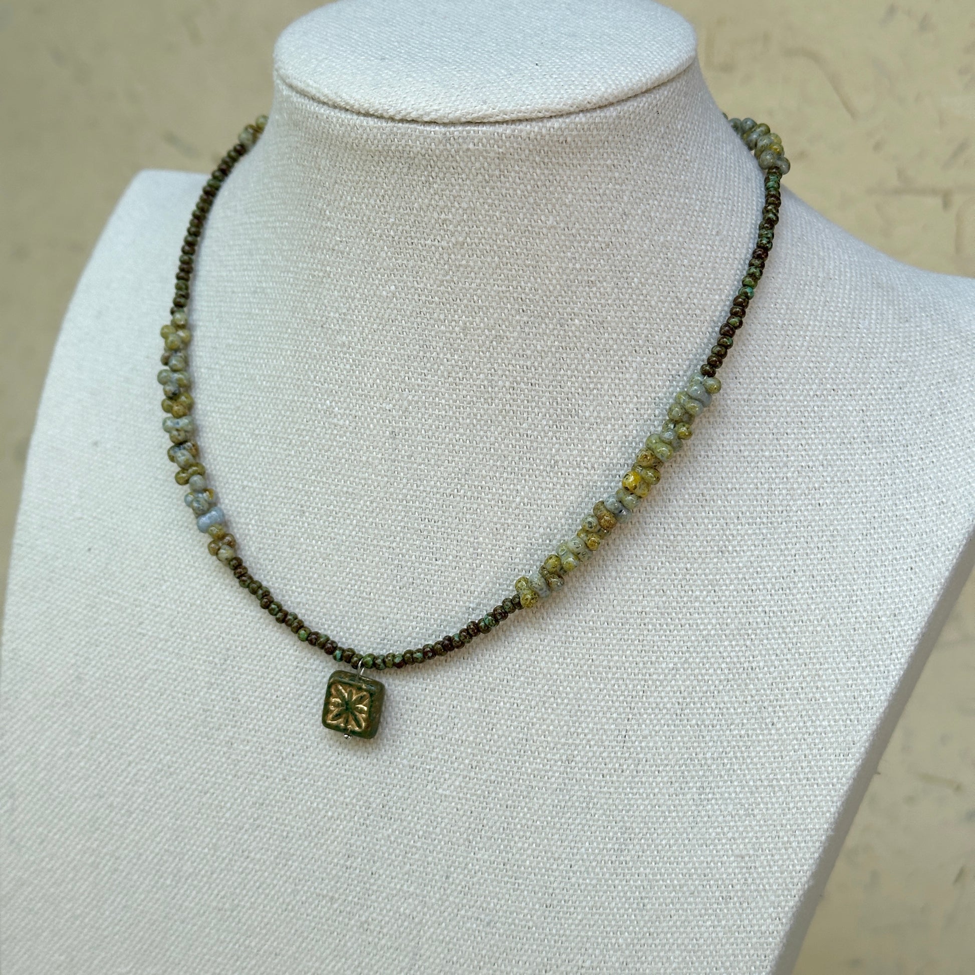 Gilded Bloom Necklace worn on bust, showing elegant golden and dark bead strand with engraved square floral charm