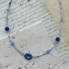 Celestial Wave Necklace flat lay on textured paper, featuring blue seed beads with central celestial-inspired pendant