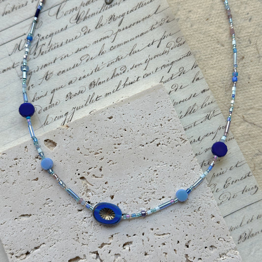 Celestial Wave Necklace flat lay on textured paper, featuring blue seed beads with central celestial-inspired pendant