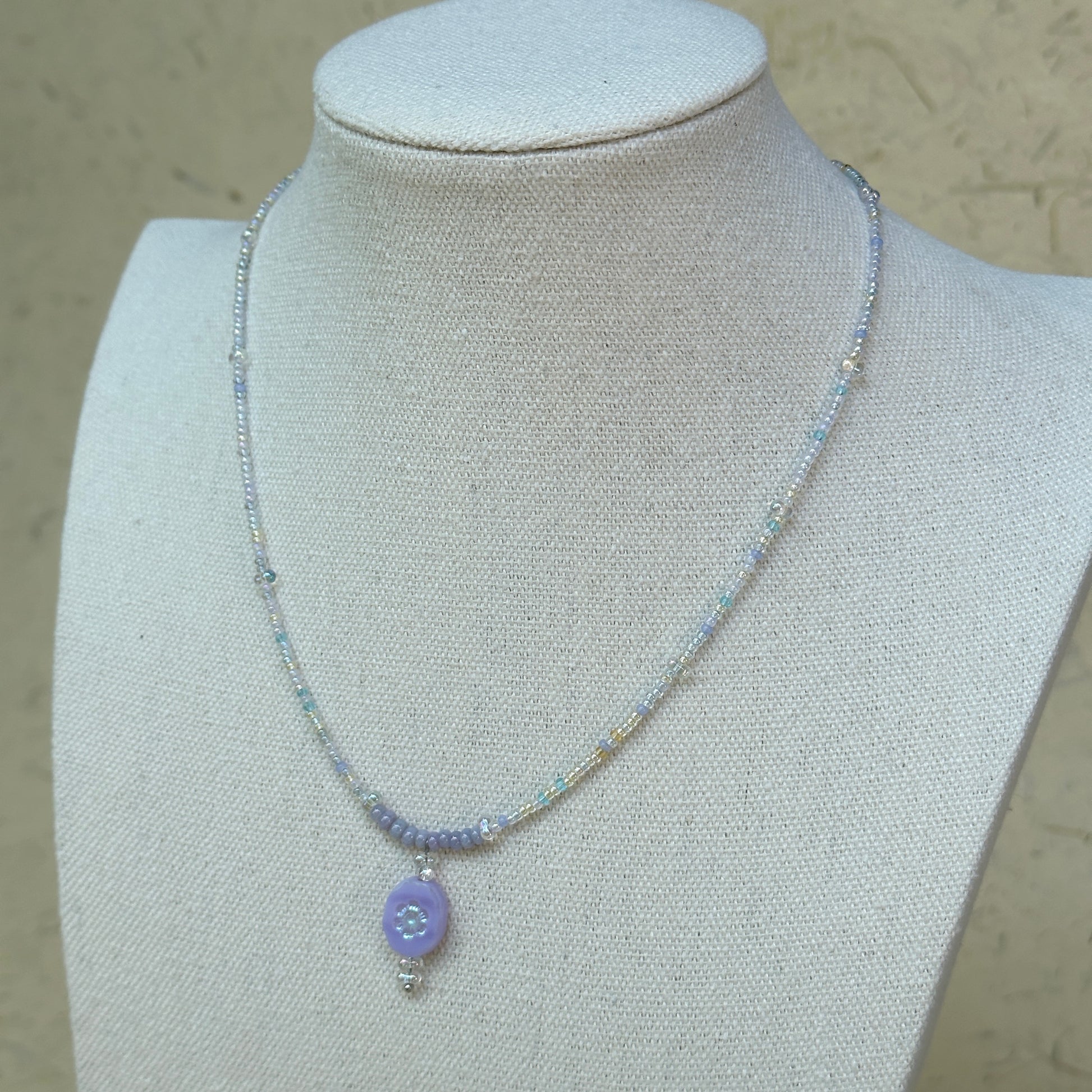 Aurora Dew Necklace displayed on bust, highlighting delicate beaded strand and glowing lavender pendant with crystal detail