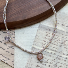 Iridescent Dew Necklace flat lay on wooden background with soft pastel glass beads and shimmering lampwork pendant