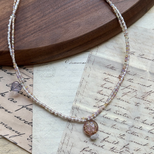 Iridescent Dew Necklace flat lay on wooden background with soft pastel glass beads and shimmering lampwork pendant