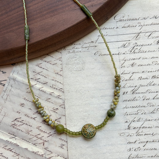 Verdant Bloom Necklace with gradient green and gold seed beads, floral medallion centerpiece, displayed on vintage paper background
