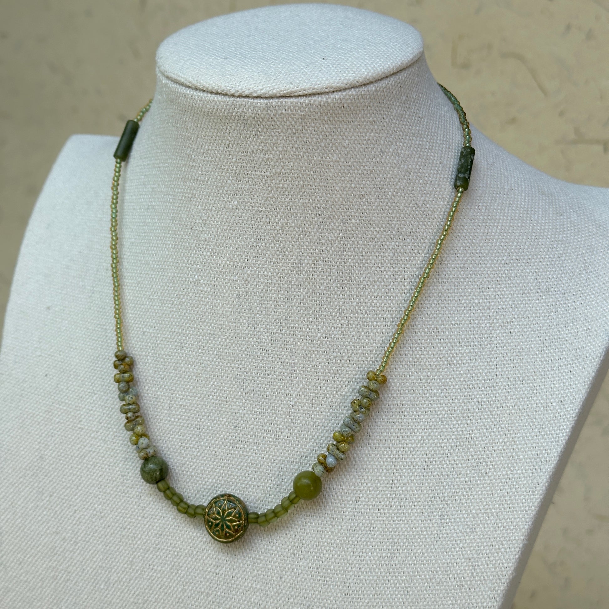 Verdant Bloom Necklace flat lay on textured paper, emphasizing handcrafted floral medallion and green bead accents