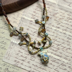 Handcrafted Autumn Whisper Necklace with amber, golden-brown, and muted blue beads, featuring floral and leaf-shaped accents, displayed on wooden background.
