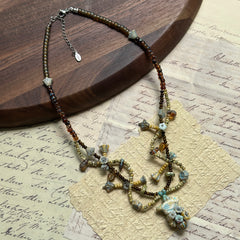 Artisan beaded necklace with amber glass, Czech beads, and leaf-inspired charms, arranged in circular form on white surface.