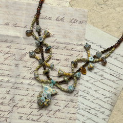 Autumn Whisper Necklace with golden-brown and soft blue tones, floral and leaf-shaped accents, shown on wooden necklace display stand.