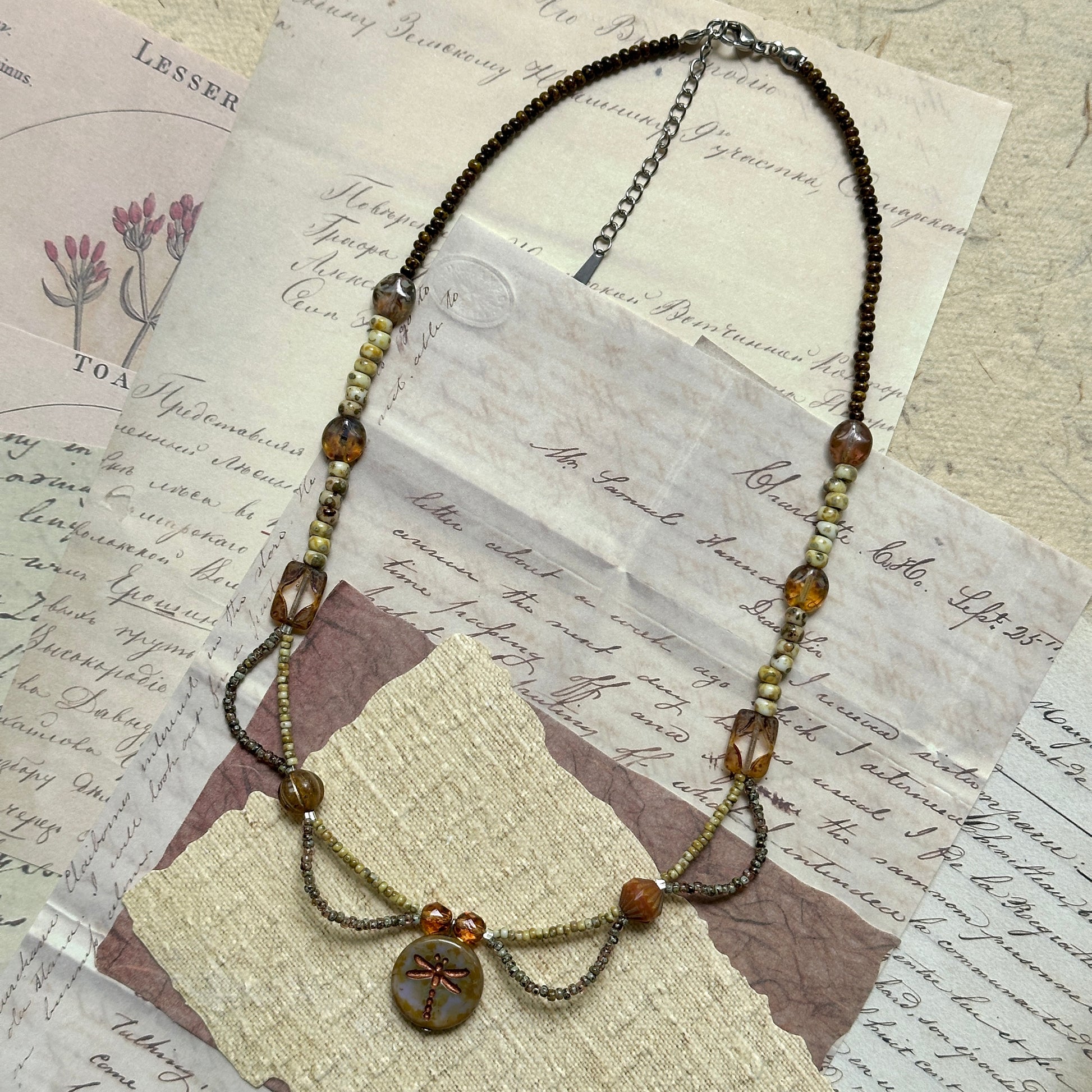 Vintage-inspired Dragonfly Whisper Necklace made of amber beads, Czech glass, and natural stones, lightweight cascading bead loops design shown flat.