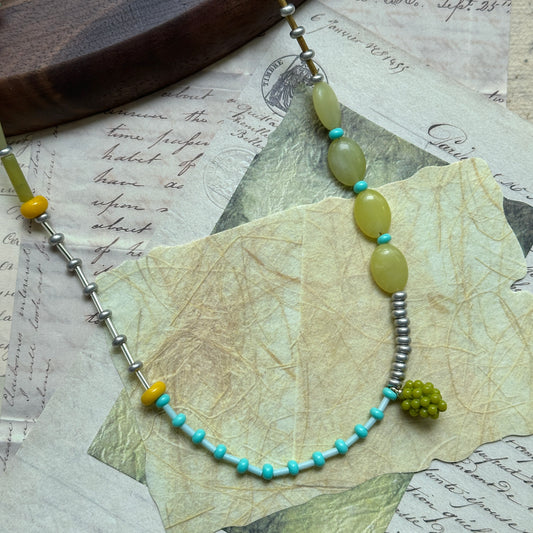 Handcrafted Vineyard Dream Necklace with olive-green, turquoise, and golden yellow beads, featuring a grape-cluster pendant, displayed on wooden background.