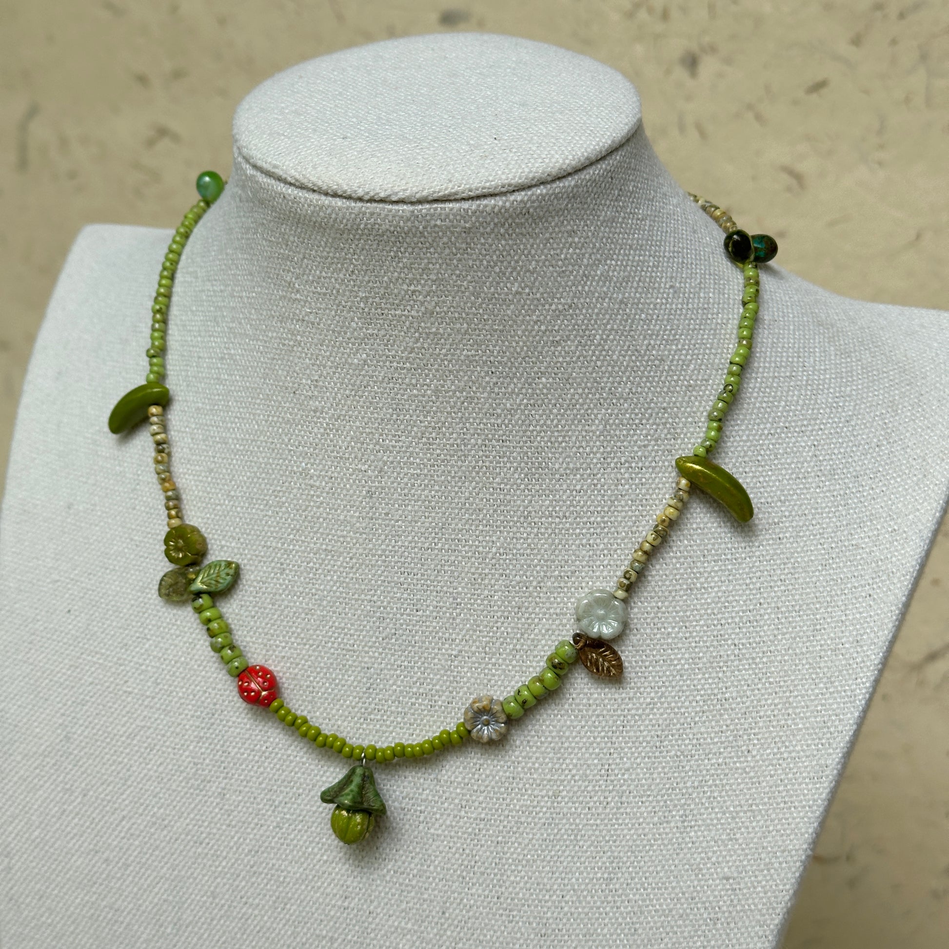 Toadstool Charm Necklace worn on white bust display, highlighting woodland details with mushroom, leaves, flowers, and red berry accent.