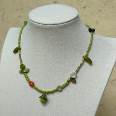 Toadstool Charm Necklace worn on white bust display, highlighting woodland details with mushroom, leaves, flowers, and red berry accent.
