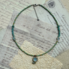 Handcrafted Lake Blossom Necklace with turquoise, golden-yellow, and earthy beads, featuring a central floral pendant with leaf accents, displayed flat on vintage background.