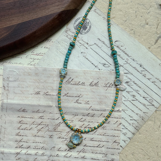 Lake Blossom Necklace with handcrafted beads in turquoise and earthy hues, floral and leaf motif, arranged in circular display on white background.
