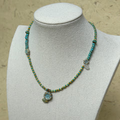 Lake Blossom Necklace worn on white bust display, highlighting turquoise beads, golden-yellow accents, and delicate floral pendant with leaf details.