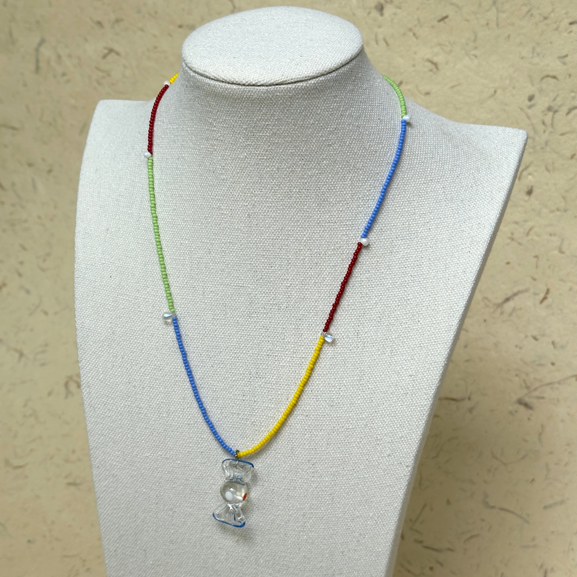 Joyful Hour Necklace worn on white bust display, highlighting rainbow seed beads and hourglass-style pendant centerpiece.