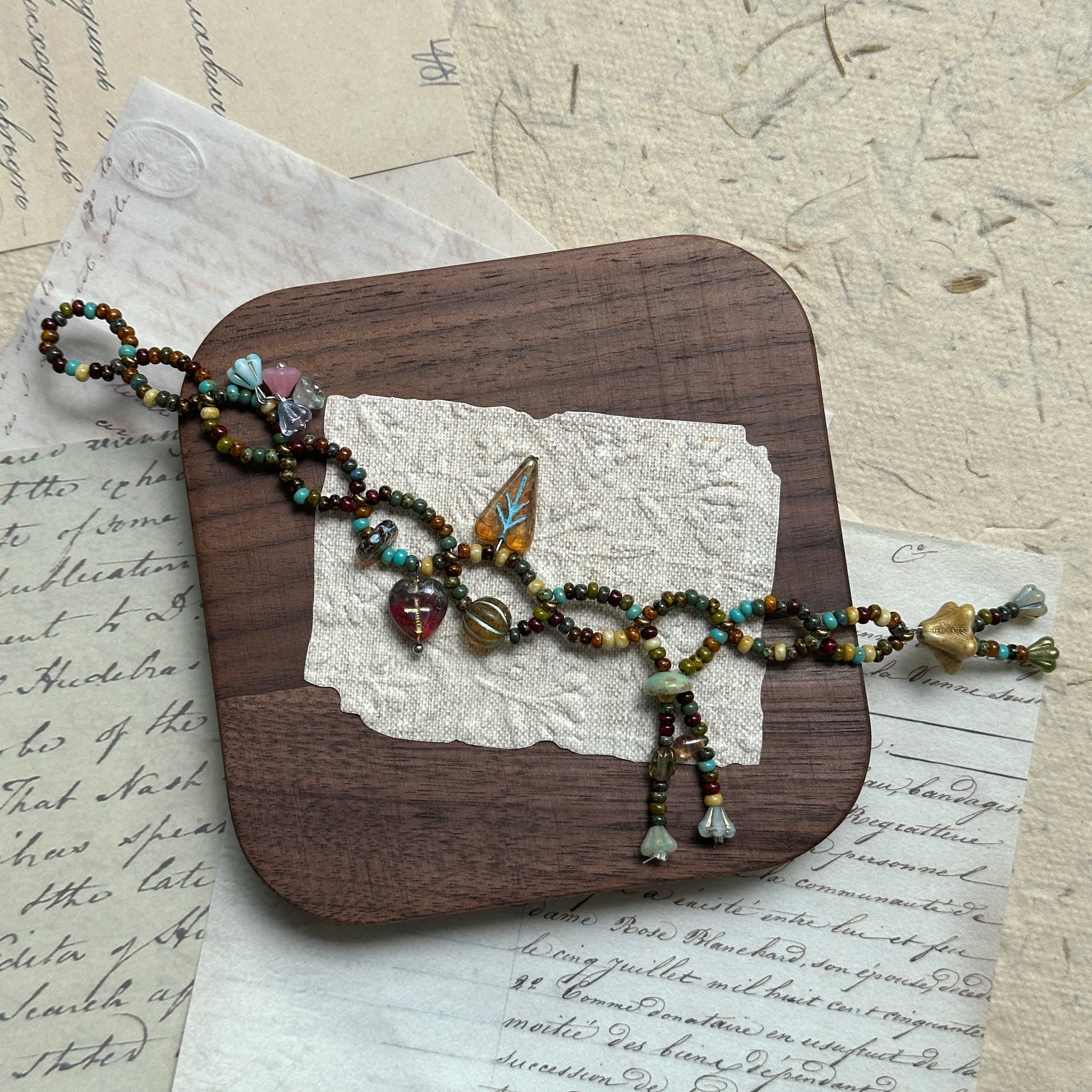 Rustic artisan bracelet in autumn tones with layered bead design, decorated with floral and leaf charms, placed on wooden surface.