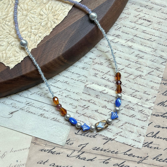 Amber Ocean Necklace — angled view on textured background, amber and sapphire-blue glass beads