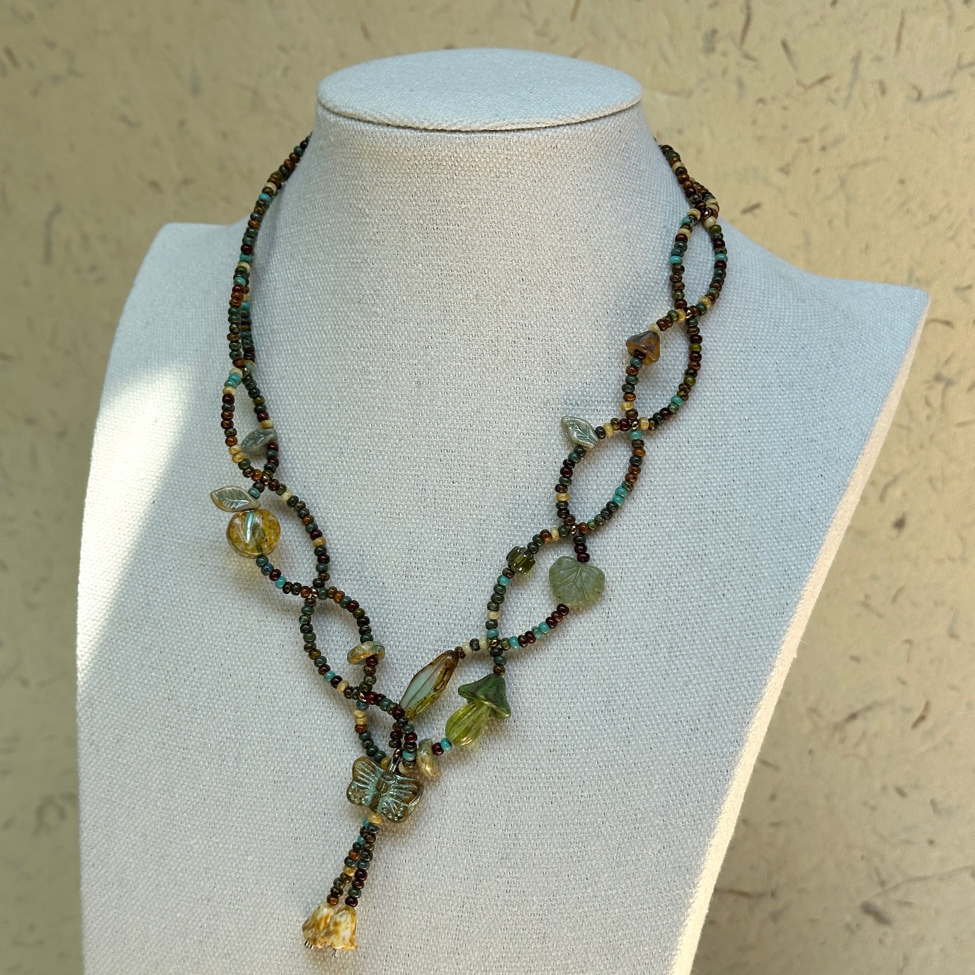 Olive Grove Lariat Necklace on a mannequin, draped lariat silhouette with adjustable drop; olive, moss and warm amber tones.