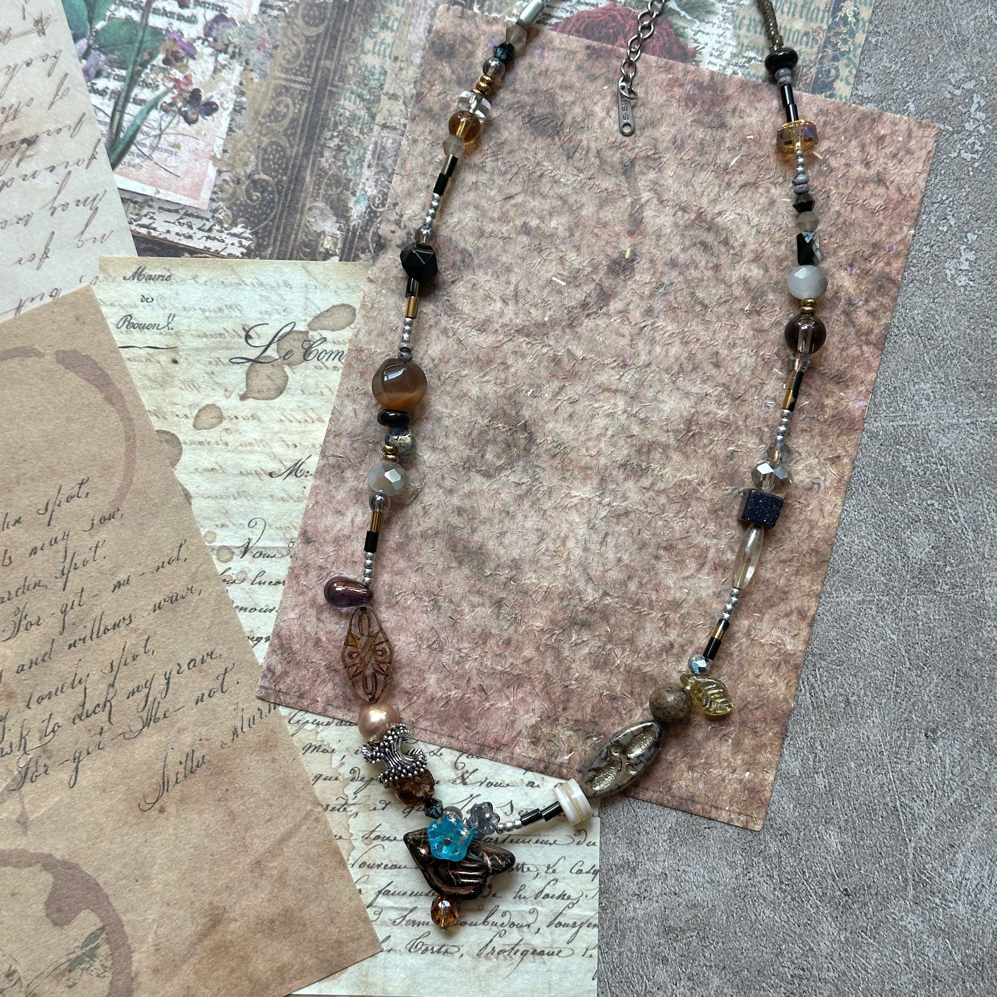 Carved motifs and pressed-glass leaf on the Nomad Relic Necklace with small stone accents; textured, intentionally asymmetric.