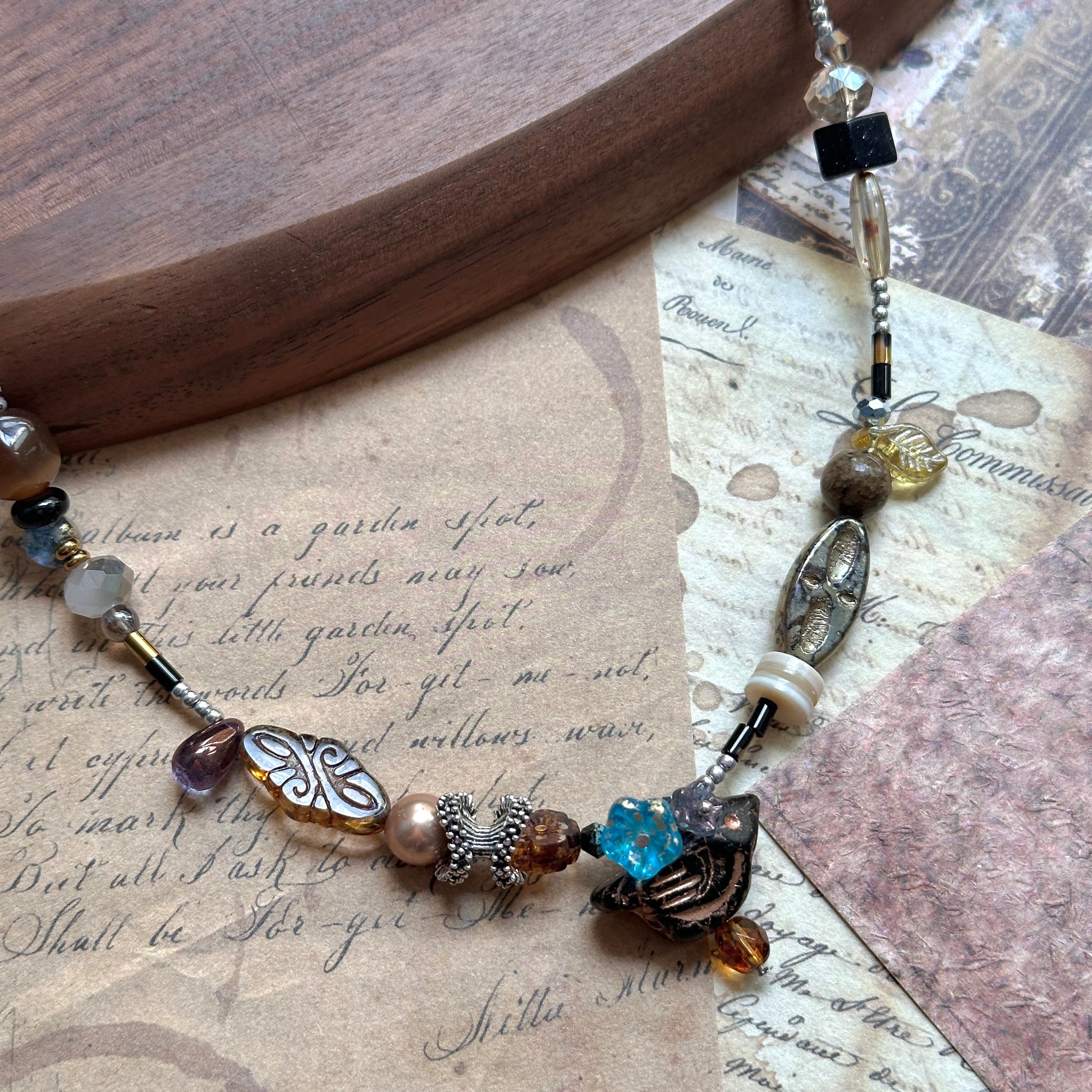 Close detail of Nomad Relic Necklace—carved leaf charm with bronze and onyx beads, Czech-glass accents, talisman look.
