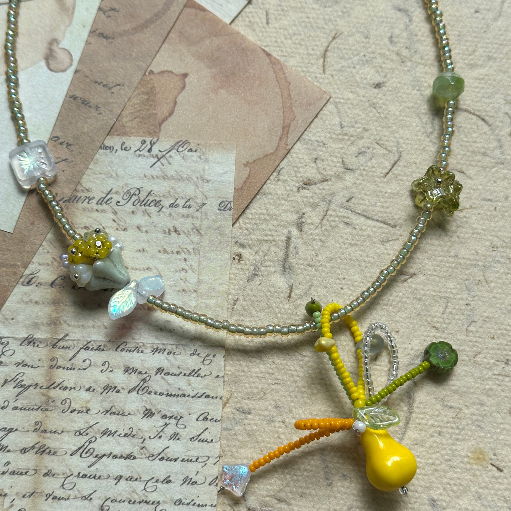 Handmade necklace with golden pear pendant and green floral glass charms on paper background – Glazenya