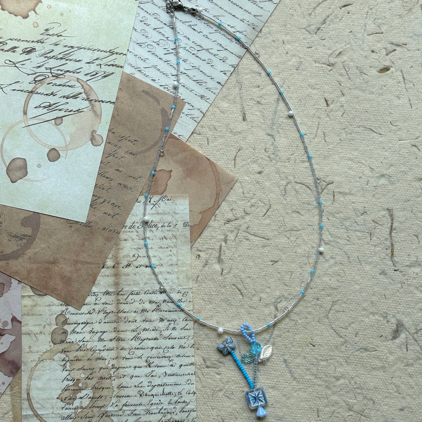 Frosted Sky Necklace coiled flat lay showing full strand and subtle asymmetry in icy blue and clear tones with delicate floral accents.