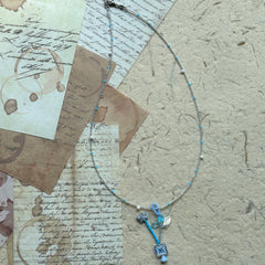 Frosted Sky Necklace coiled flat lay showing full strand and subtle asymmetry in icy blue and clear tones with delicate floral accents.