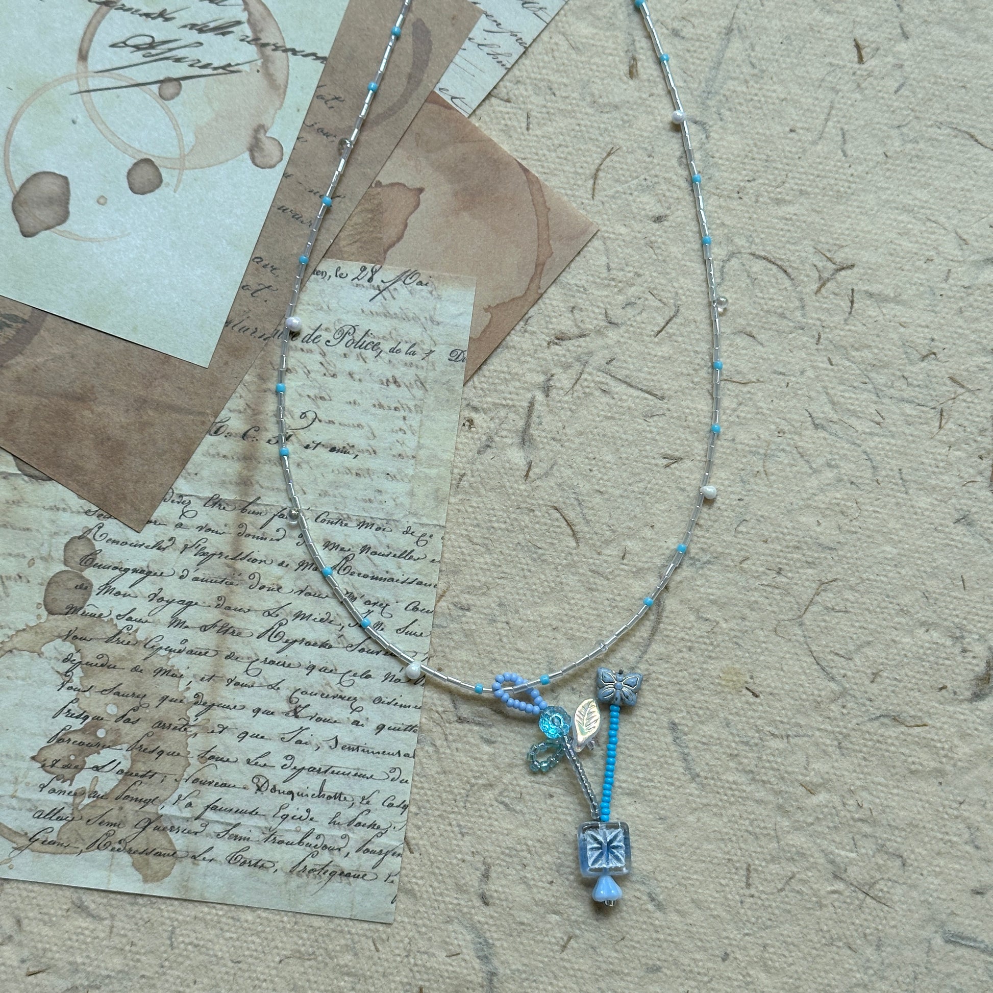 Angled flat lay highlighting crystal drops and frosted flower charms on the Frosted Sky Necklace; lightweight, luminous feel.