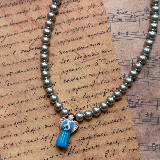 Close detail of Angel’s Grace Necklace—luminous faux-pearl strand with sky-blue glass angel charm pendant.