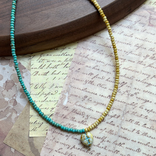 Close detail of the Faithlight Necklace—two-tone strand, half amber yellow and half teal green, lightweight hand-strung beads on wood.
