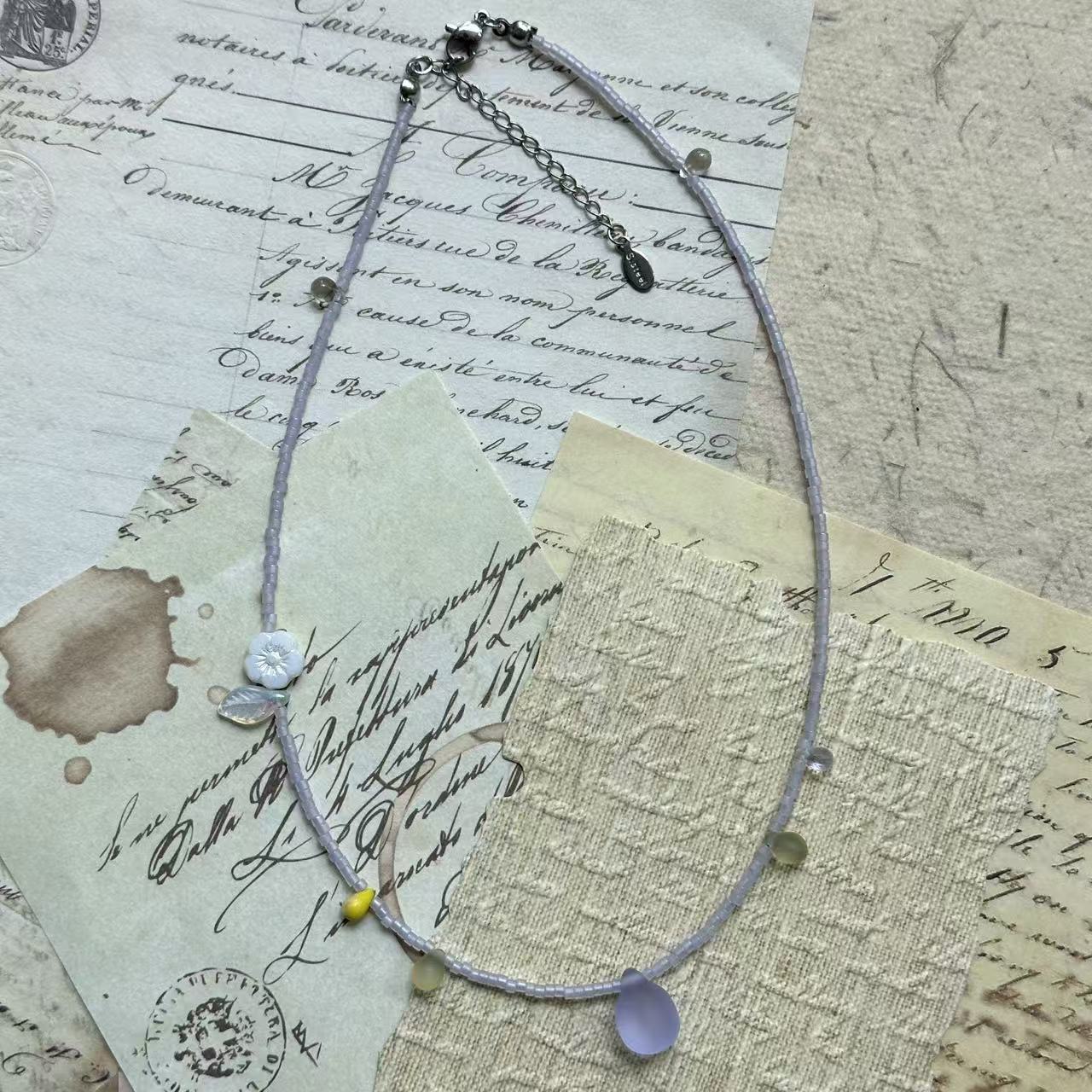 Pendant close-up: frosted lilac glass teardrop surrounded by tiny lavender seed beads and subtle spring accents.