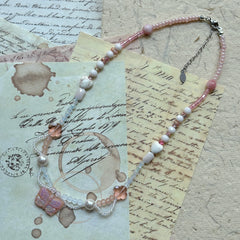Pendant close-up on vintage paper—rose-pink Czech-glass butterfly with ivory seed-bead swags, faceted crystals and pearl accents.