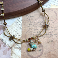 Close detail of Woodland Spirit Necklace—turquoise glass leaf pendant with Czech-glass flower accents and earthy amber/brown beads; flat lay.