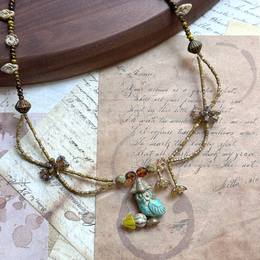 Close detail of Woodland Spirit Necklace—turquoise glass leaf pendant with Czech-glass flower accents and earthy amber/brown beads; flat lay.