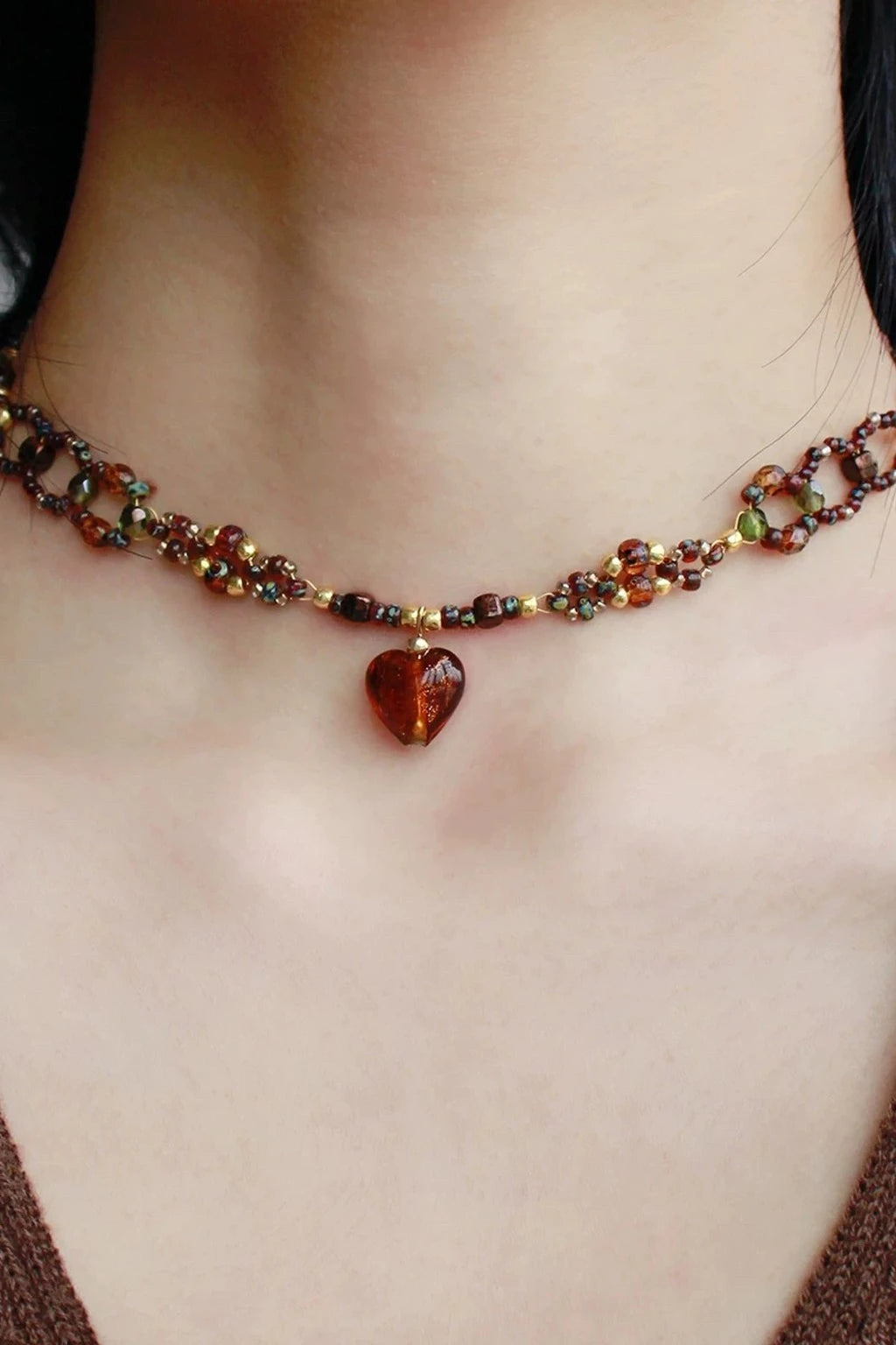 wearing a minimalist mixed-bead choker with curved silver tube segments and wood/amber/black beads plus a tiny lime accent, shown against a black backdrop and white off-shoulder top.
