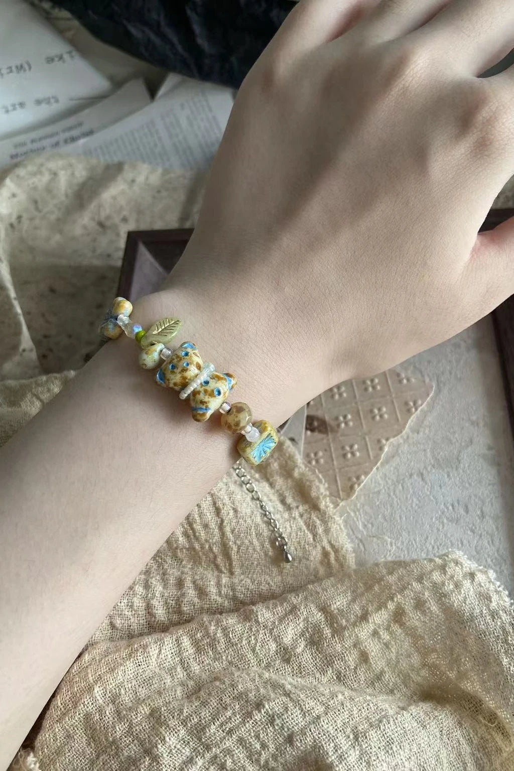 Customer’s wrist wearing a handcrafted beaded bracelet in yellow and turquoise with a small leaf charm, photographed in natural light on linen.
