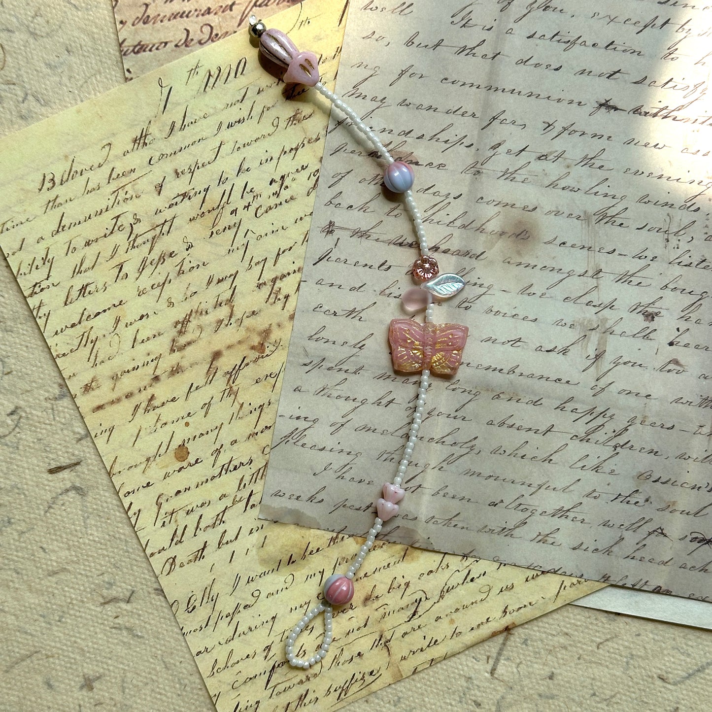 Close view of bracelet on paper background, petite flowers, leaf charm, and striped pink round beads in soft blush and rose tones